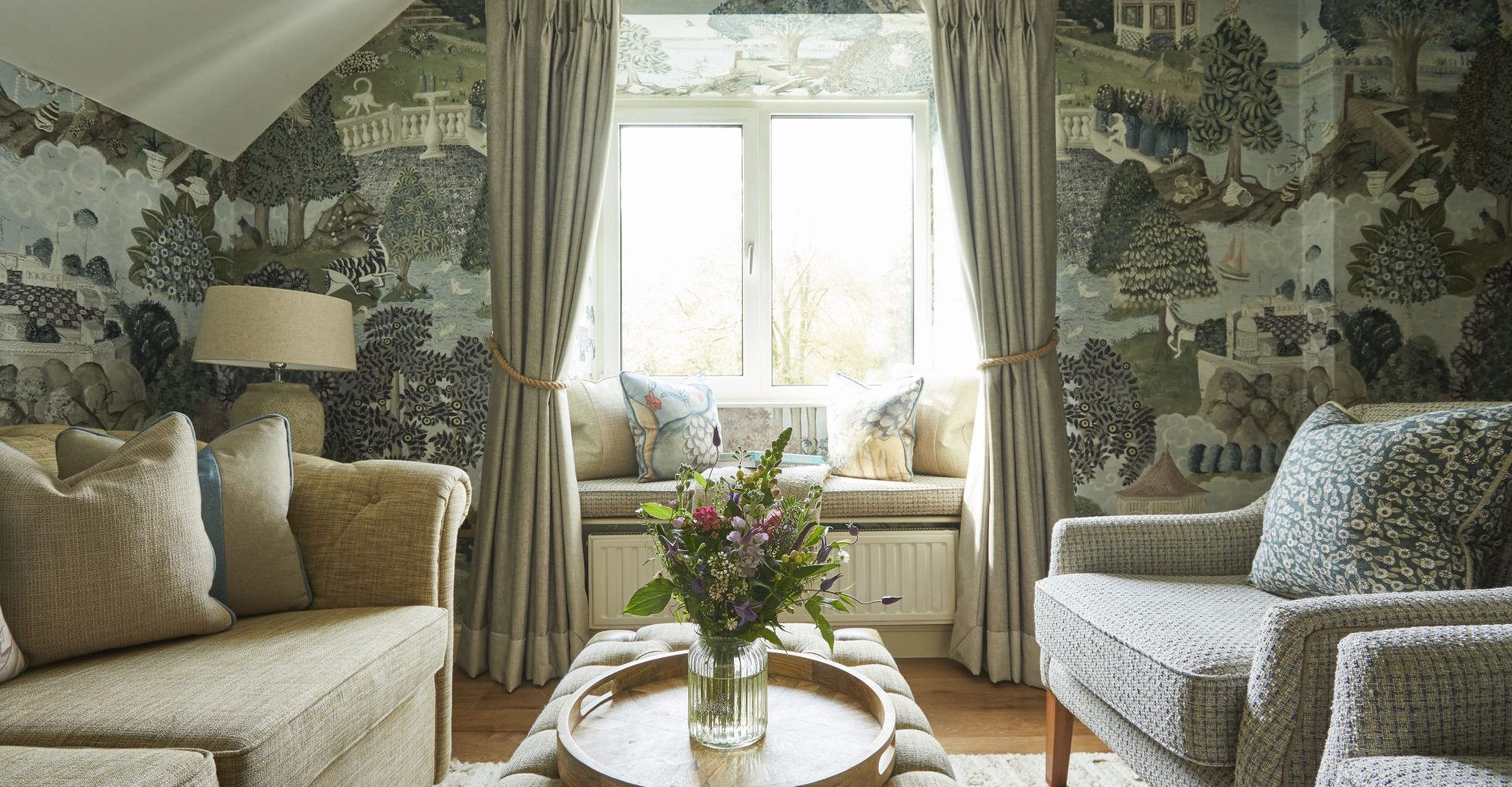 A bright and inviting living space with soft beige sofas, colourful cushions, and a centrepiece bouquet at Rothay Manor.