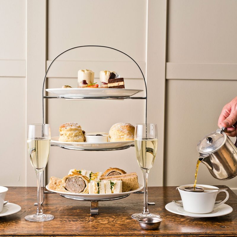 Afternoon tea setup at Rothay Manor Hotel with a tiered tray of sandwiches, scones, and desserts, champagne flutes, and tea.